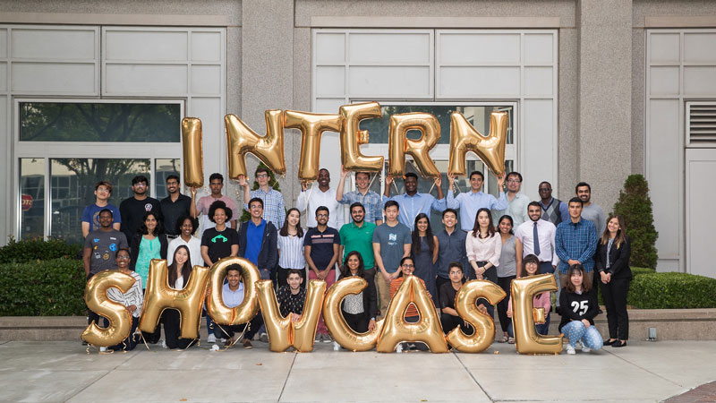 A group of interns hold balloons that spell out the words “Intern Showcase”.