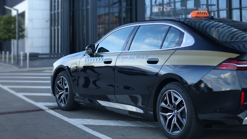 A sleek black taxi with a roof sign is parked on a city street, reflecting modern glass buildings.