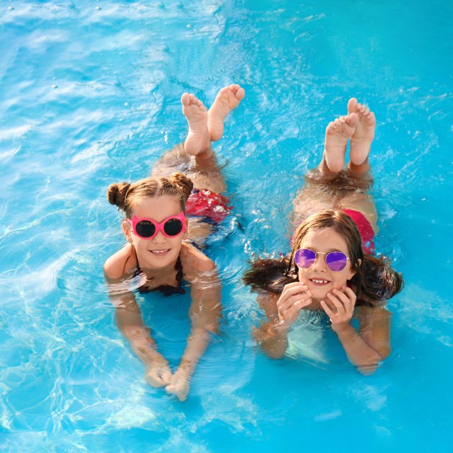 Two children joyfully float in a pool, wearing colorful sunglasses.