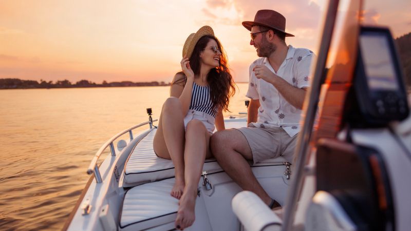 A couple relaxes on a boat at sunset, smiling and enjoying the view.