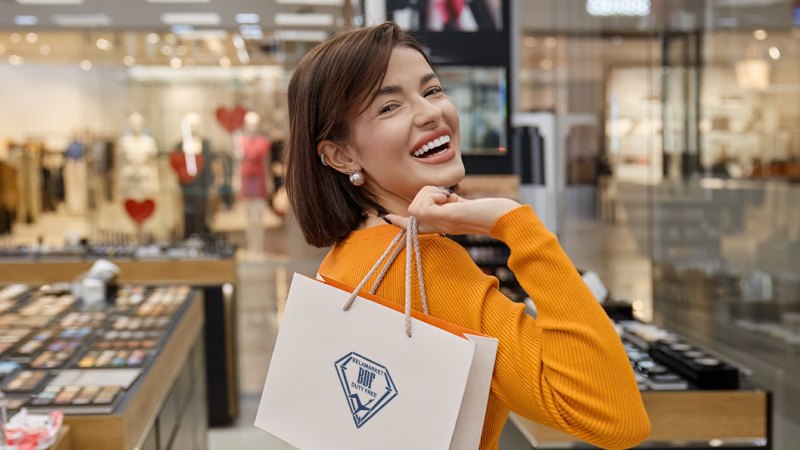 Улыбающаяся женщина в оранжевом свитере стоит с сумкой для покупок в торговом центре