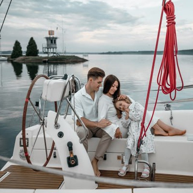 Семья сидит на яхте на закате, на фоне спокойной воды и небольшого острова.