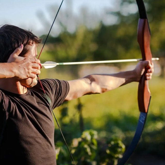 Человек в черной рубашке ловко натягивает тетиву, нацеливая стрелу на невидимую цель.