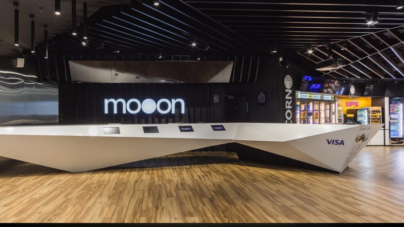 Просторная современная зона приема с элегантным белым столом с четкими углами на темном фоне. На стене светится надпись «Moon».