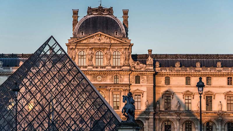 Glass pyramid and historic Louvre Museum building in Paris, France, illuminated by sunlight.