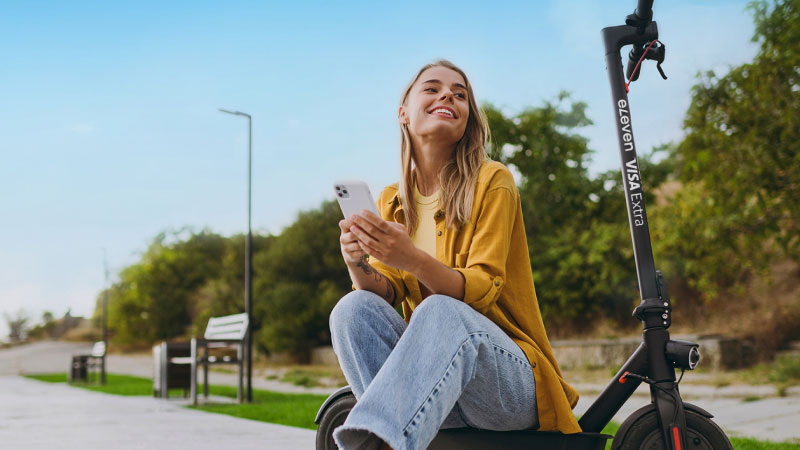 Woman sitting on e-scooter using smartphone outdoors